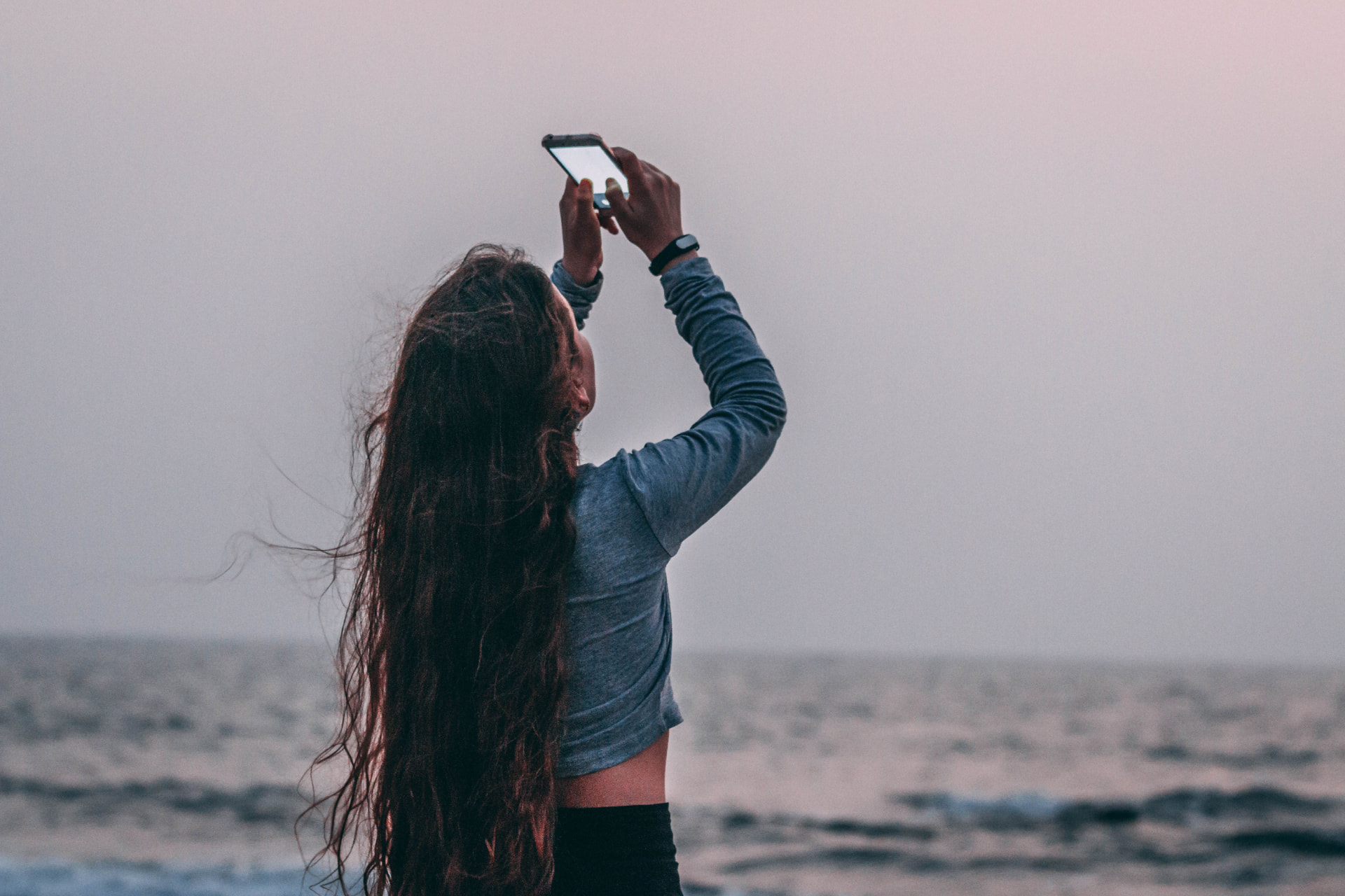 A woman capturing a moment by the ocean on her phone
